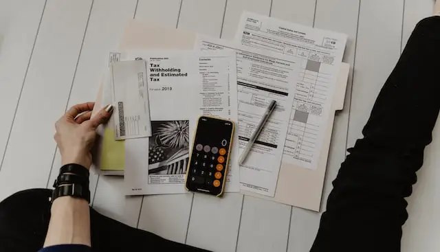 An image of a person holding a calculator, with a pile of cryptocurrency-related documents.